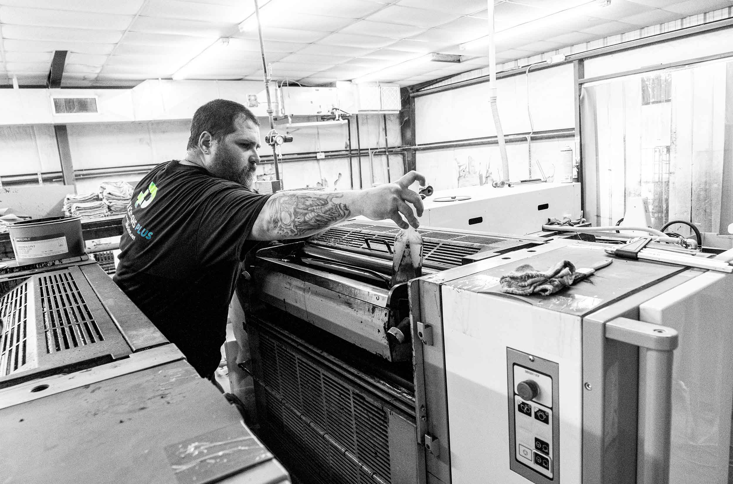 Man operating sheet-fed printing press.